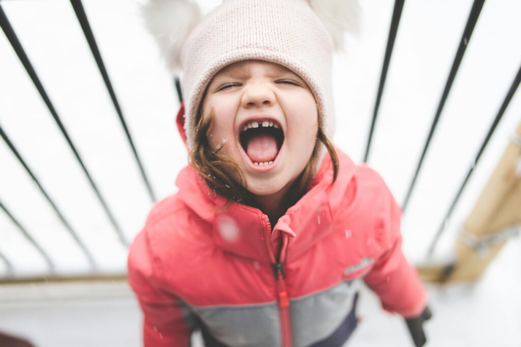 Cheerful child wearing winter clothing screams happily in the snowy outdoors.